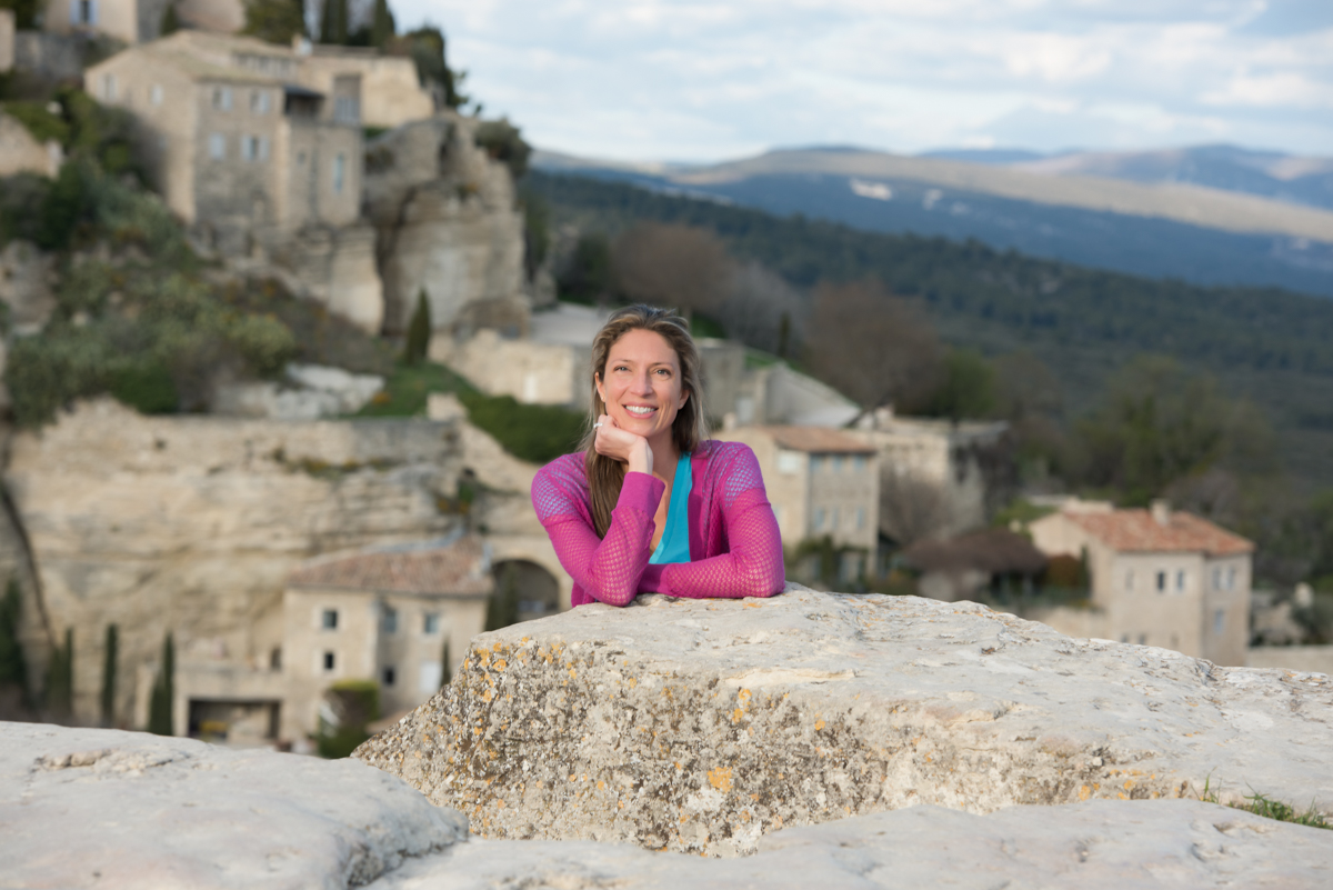 Emily Durand, chauffeur-guide of Your Private Provence, posing in front of the hilltop village of Gordes, a symbol of Provençal heritage