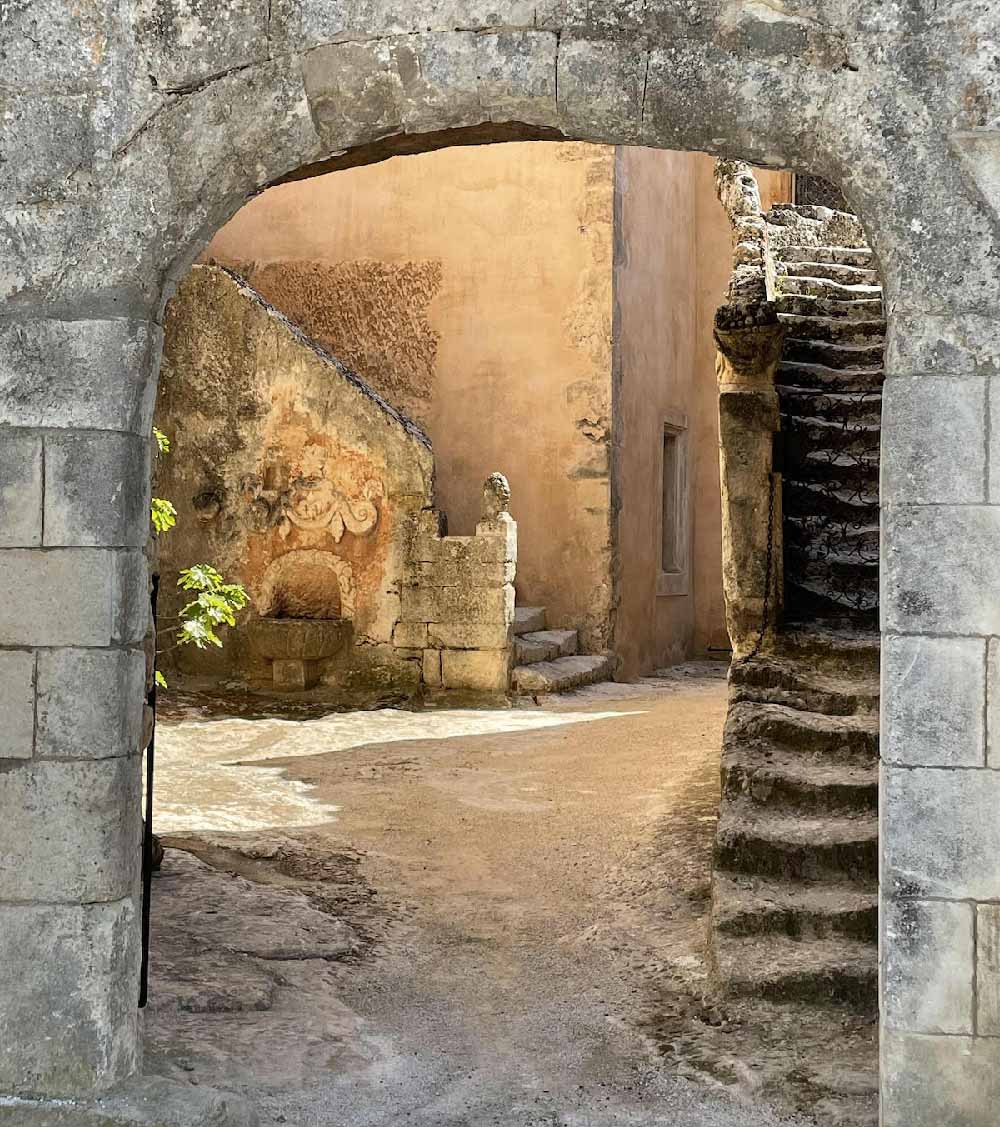 Stone archway leading to a picturesque courtyard with an ancient staircase at Château de Mille in Apt.