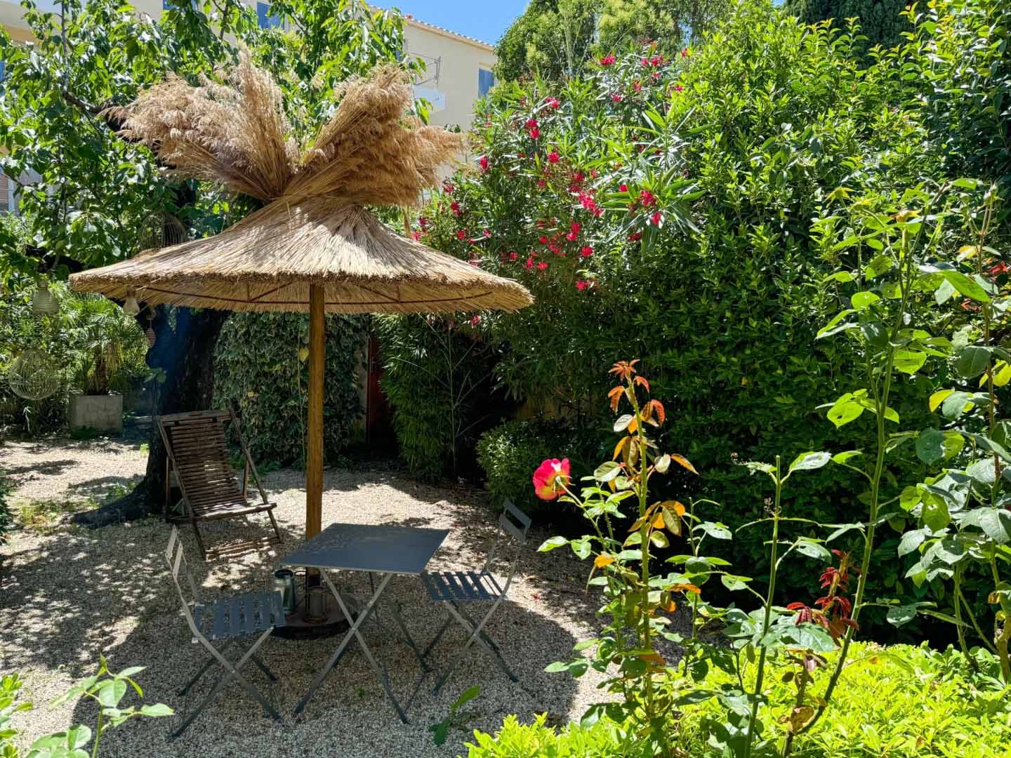 Peaceful garden at Nid d'Ange en Provence A shaded relaxation area in the lush garden of Nid d'Ange en Provence, featuring a table and chairs under a bamboo pergola.