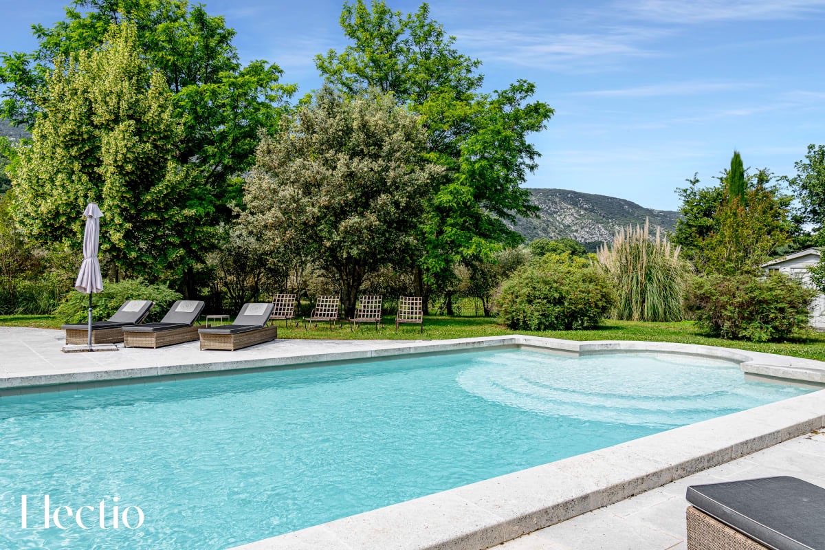 Heated pool at Résidence Les Petitons in Oppède-le-Vieux, surrounded by sun loungers and greenery with a view of the Luberon hills