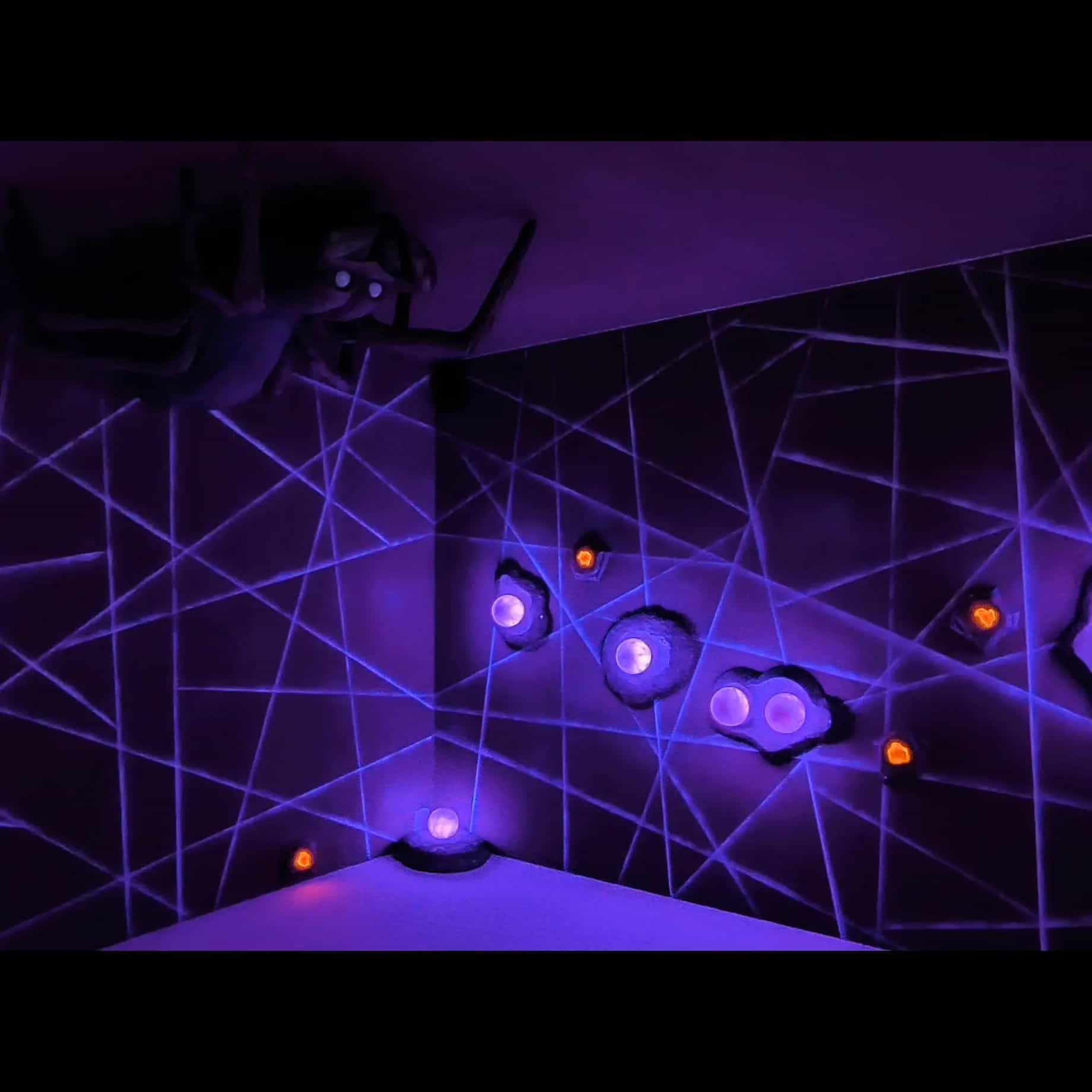 Dark game room lit by UV lights with wall-based challenges at Last Adventures