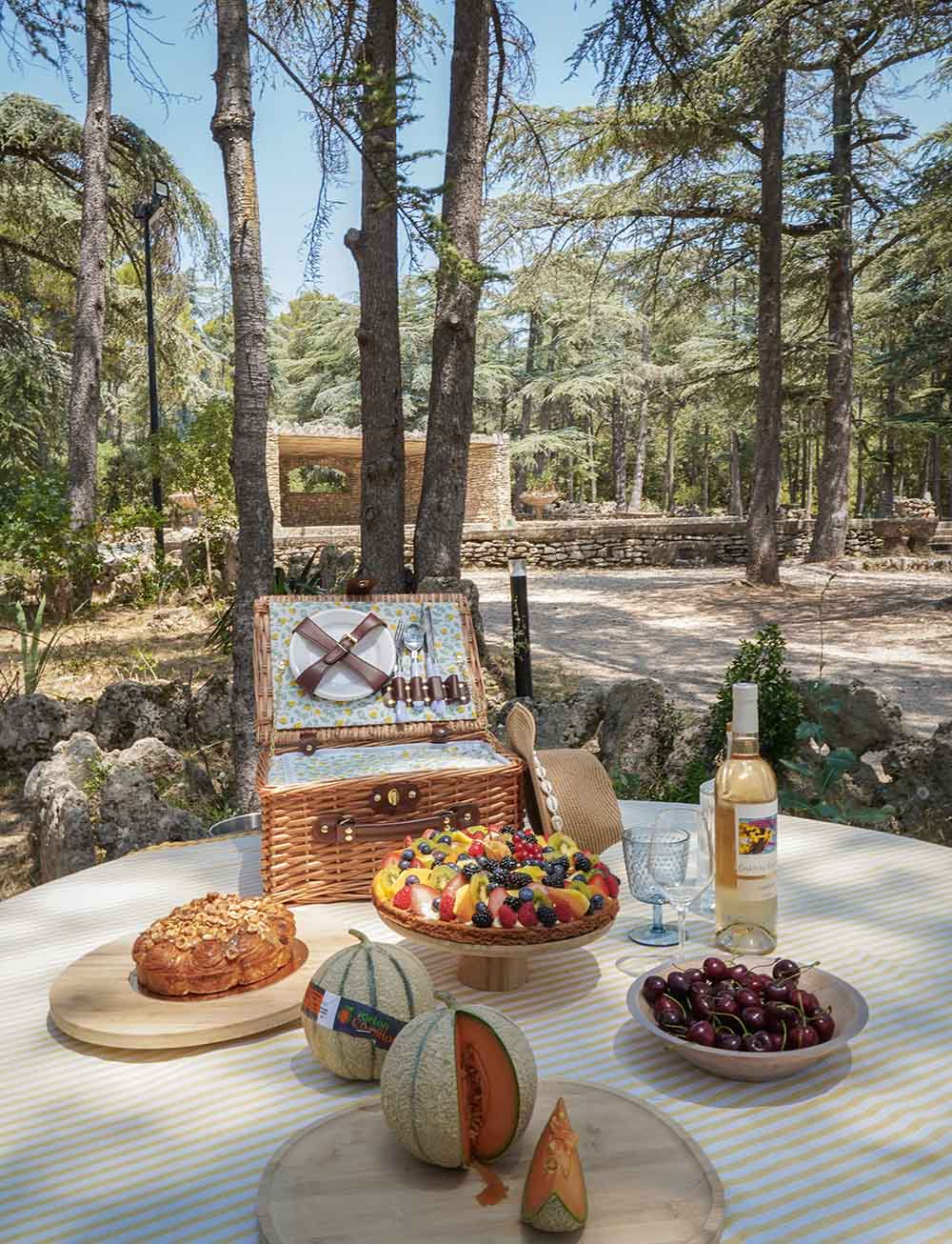 The perfect basket for a delicious local picnic Close-up of a picnic table laid with a fresh fruit tart, melon, cherries, a bottle of rosé wine and an open wicker basket.