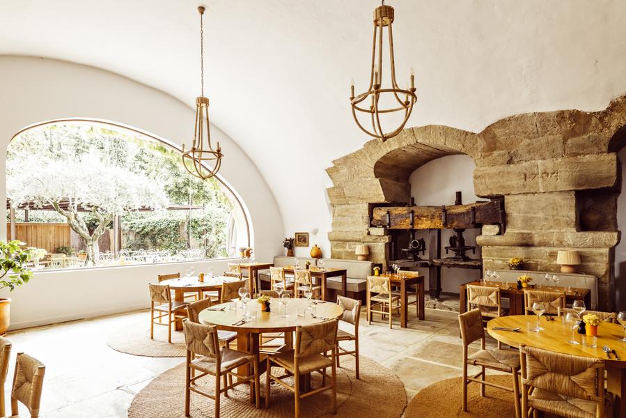Dining room of Bacheto restaurant in Lourmarin with set tables and historic stone fireplace