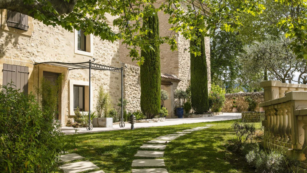 Entrance of Mas de Guilles in Lourmarin, a charming stone hotel surrounded by cypress trees and a Provençal garden in the Luberon