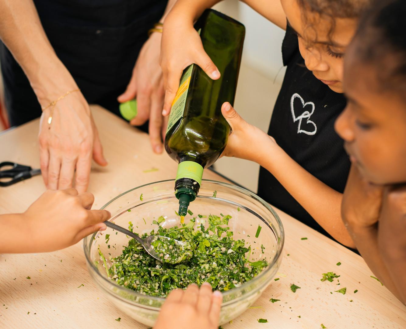 Children preparing a recipe with fresh herbs and oil during a cooking workshop exploring flavours at Festival Confit!