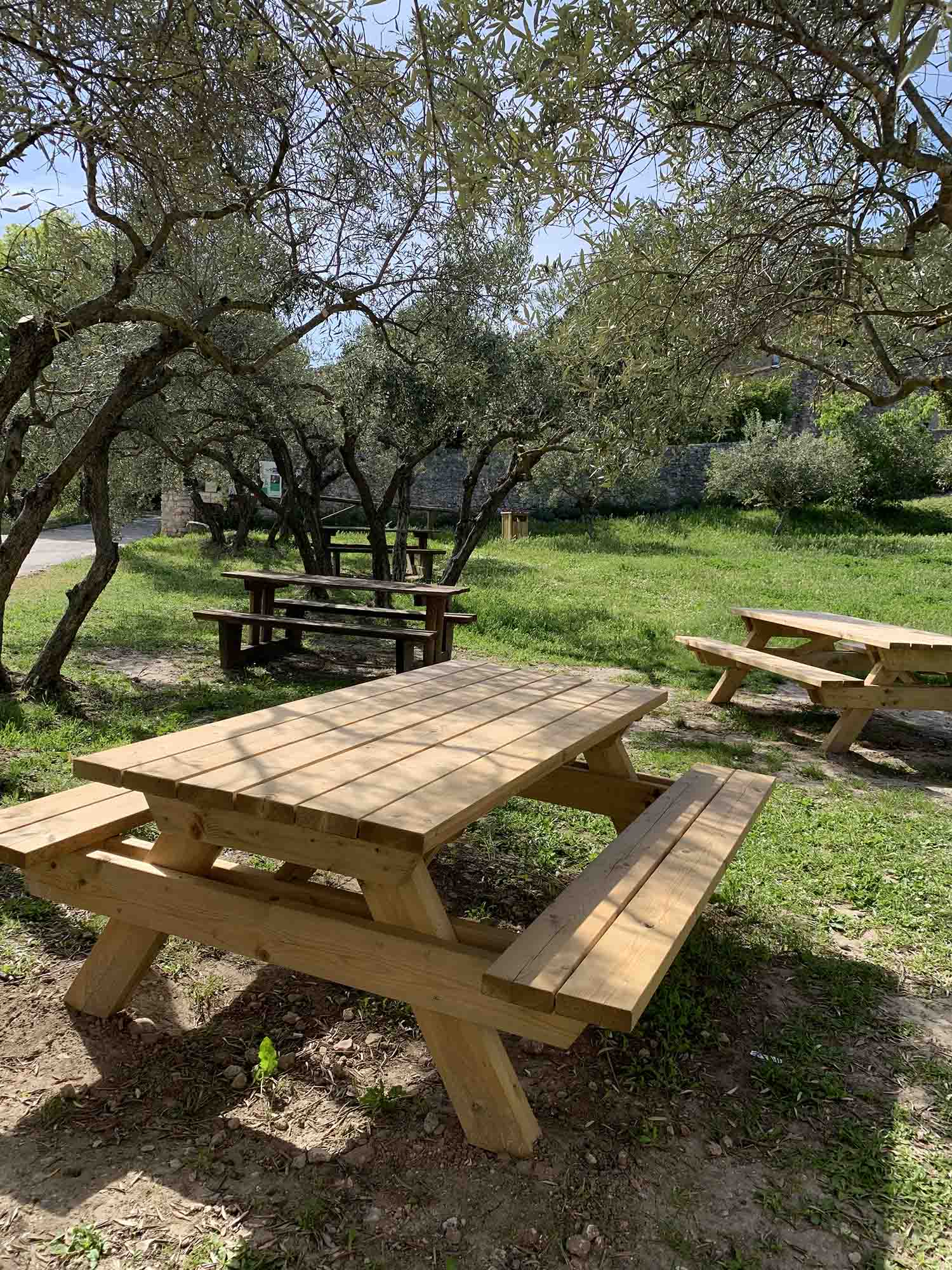 A relaxing shaded break in Mérindol’s unspoilt natural setting Two large double wooden picnic tables set on a designated gravel area, in the shade of holm oaks in the Garrigue Natural Area.