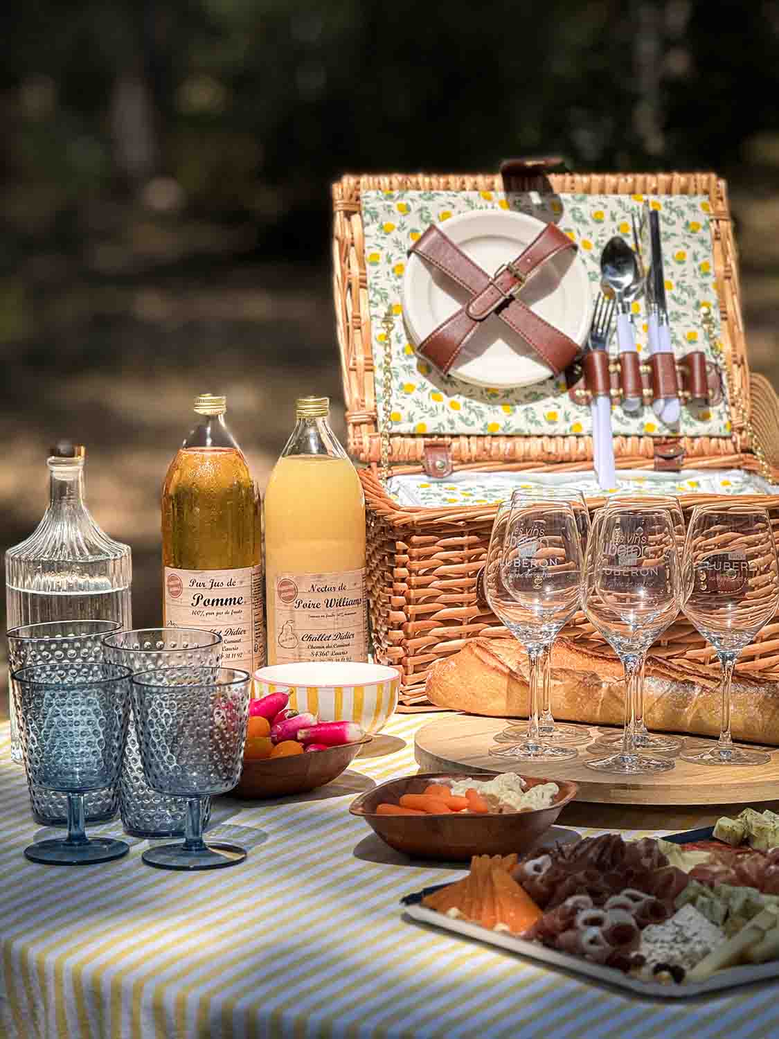 Wicker picnic basket filled with glasses and bottles on a checked blanket