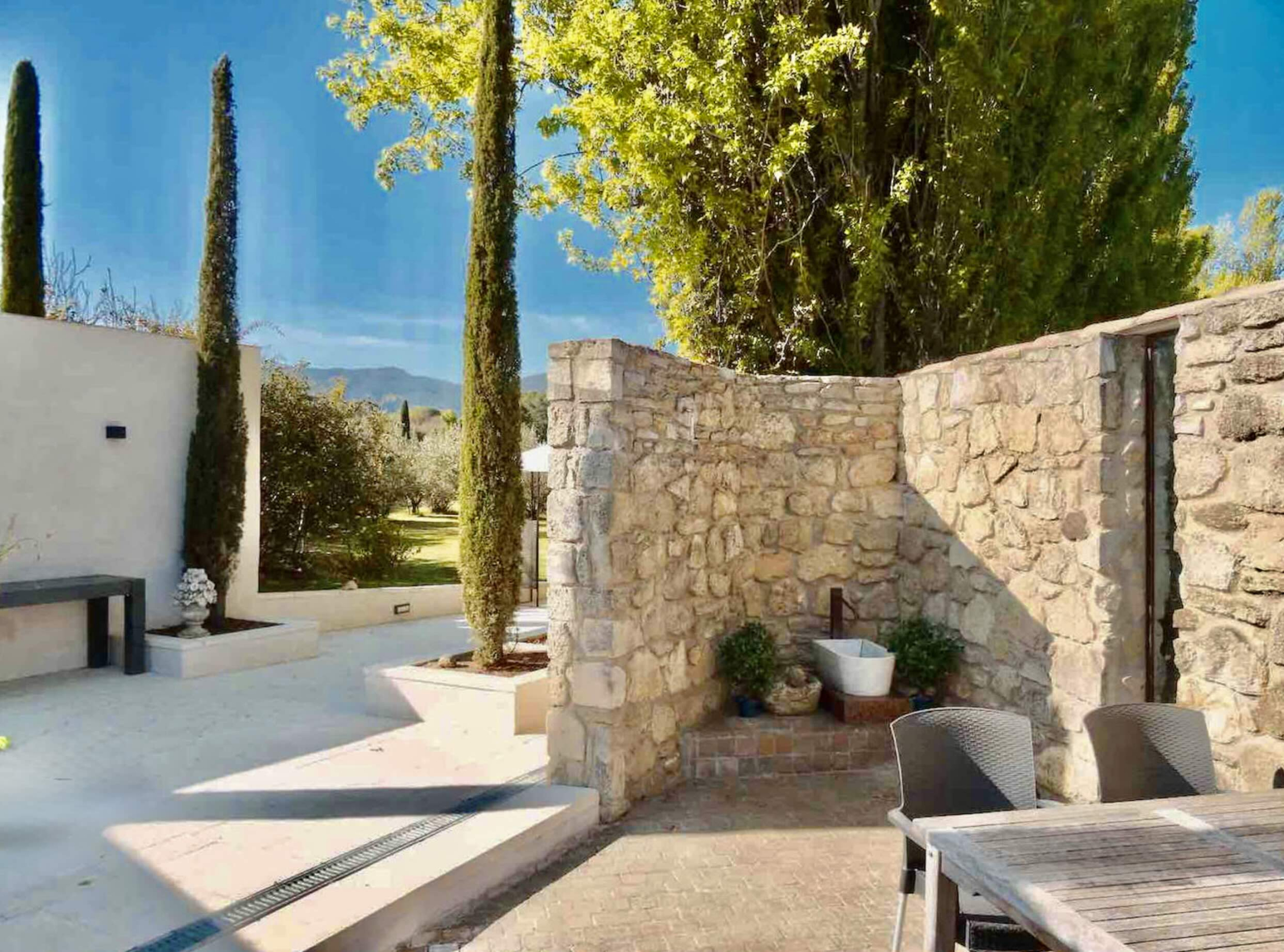 Private terrace and Provençal architecture, Les Oliviers house in Oppède Private terrace of Les Oliviers house in Oppède, with stone walls, cypress trees and relaxation areas in a peaceful Luberon setting
