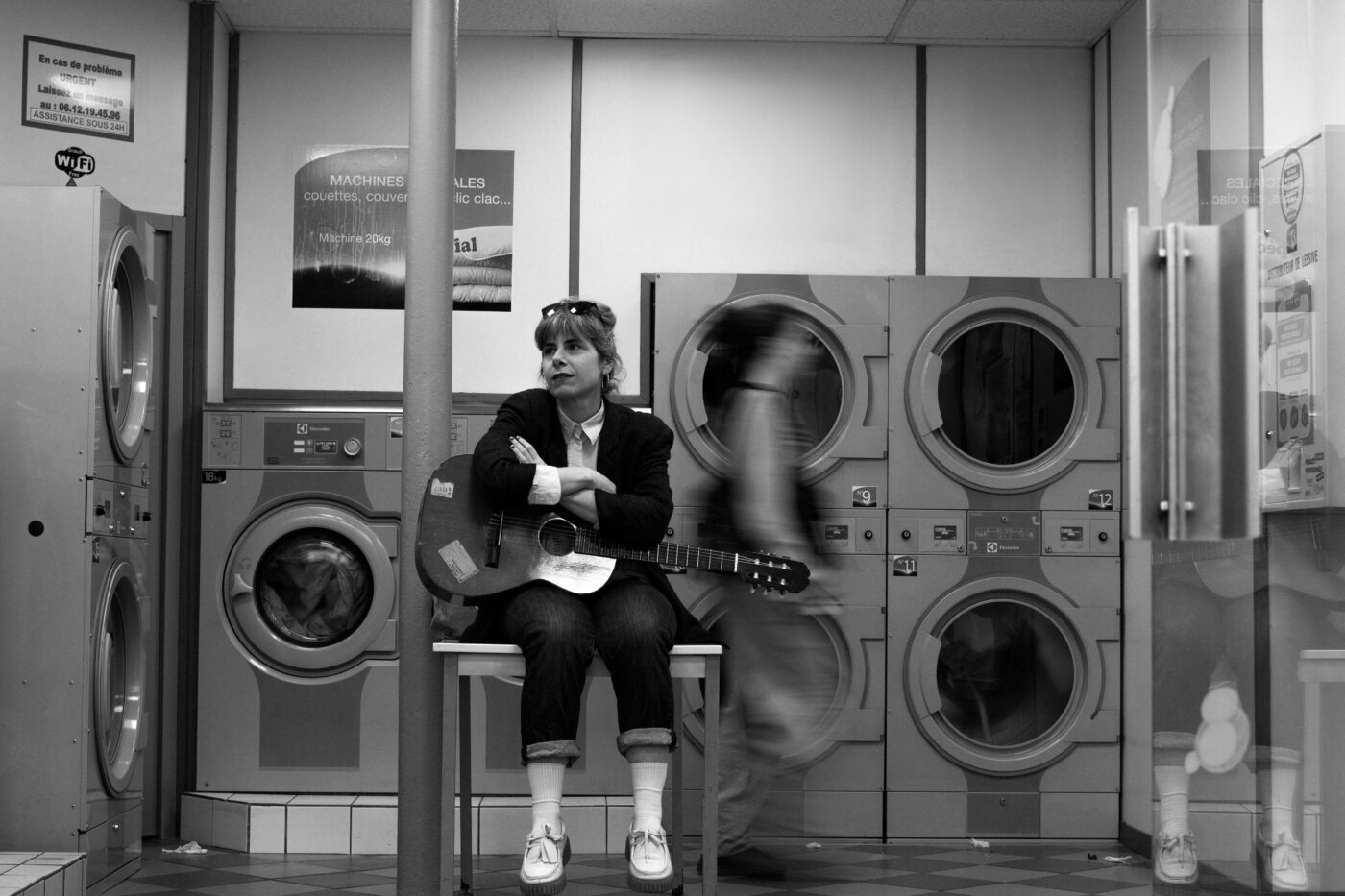 Black-and-white portrait of singer Marina P sitting with a guitar in a laundrette