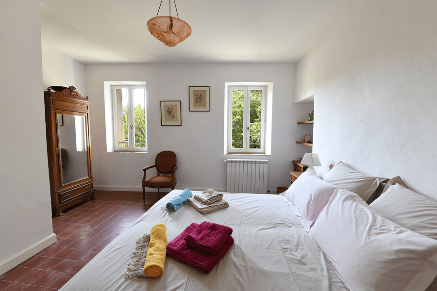 Bright and elegant bedroom at the Mas du Péressier, featuring a double bed, colorful towels, and an antique wardrobe.