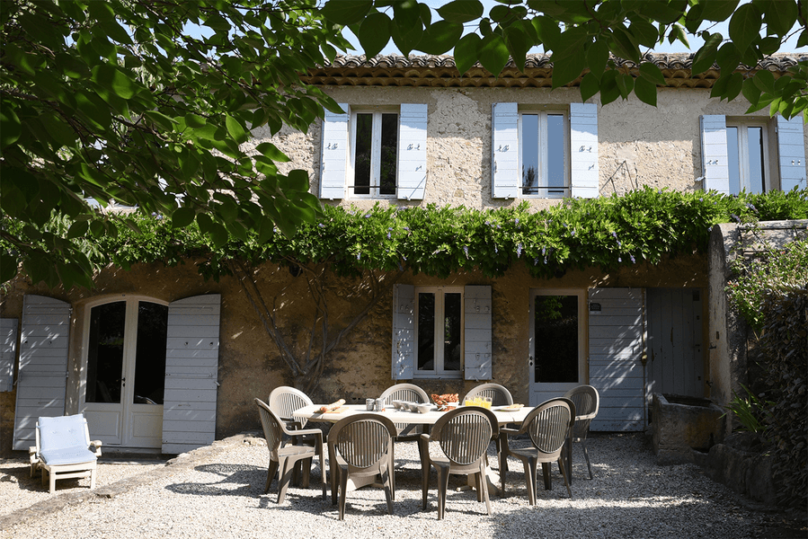 Outdoor courtyard of the Mas du Péressier, featuring a large table under a lush green pergola, in a typical Luberon setting.
